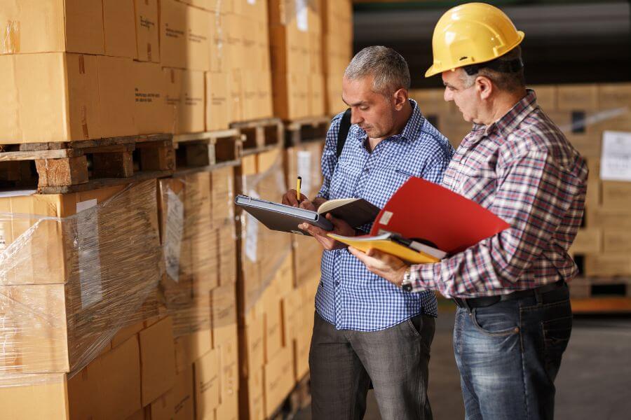 MSLC warehouse staff wearing safety gear discussing logistics operations inside modern storage facility.